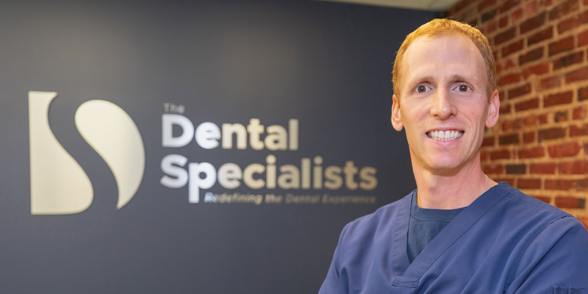 Dr. Noah P. Orenstein smiling in front of The Dental Specialists office logo