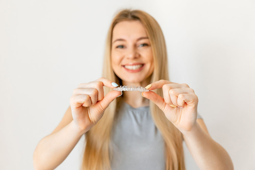 Smiling patient holding clear aligners